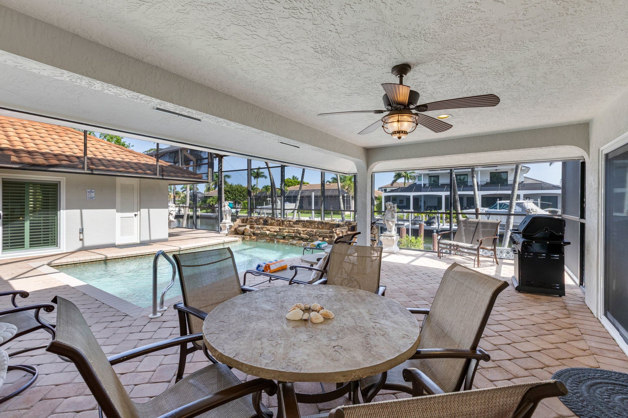 Covered lanai with outdoor dining table, ceiling fan and gas grill