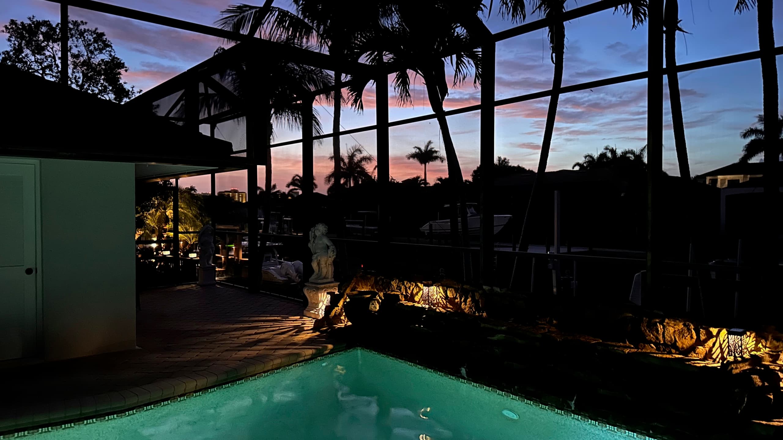 Heated pool and rock waterfall lit at dusk under the screened lanai, canal beyond