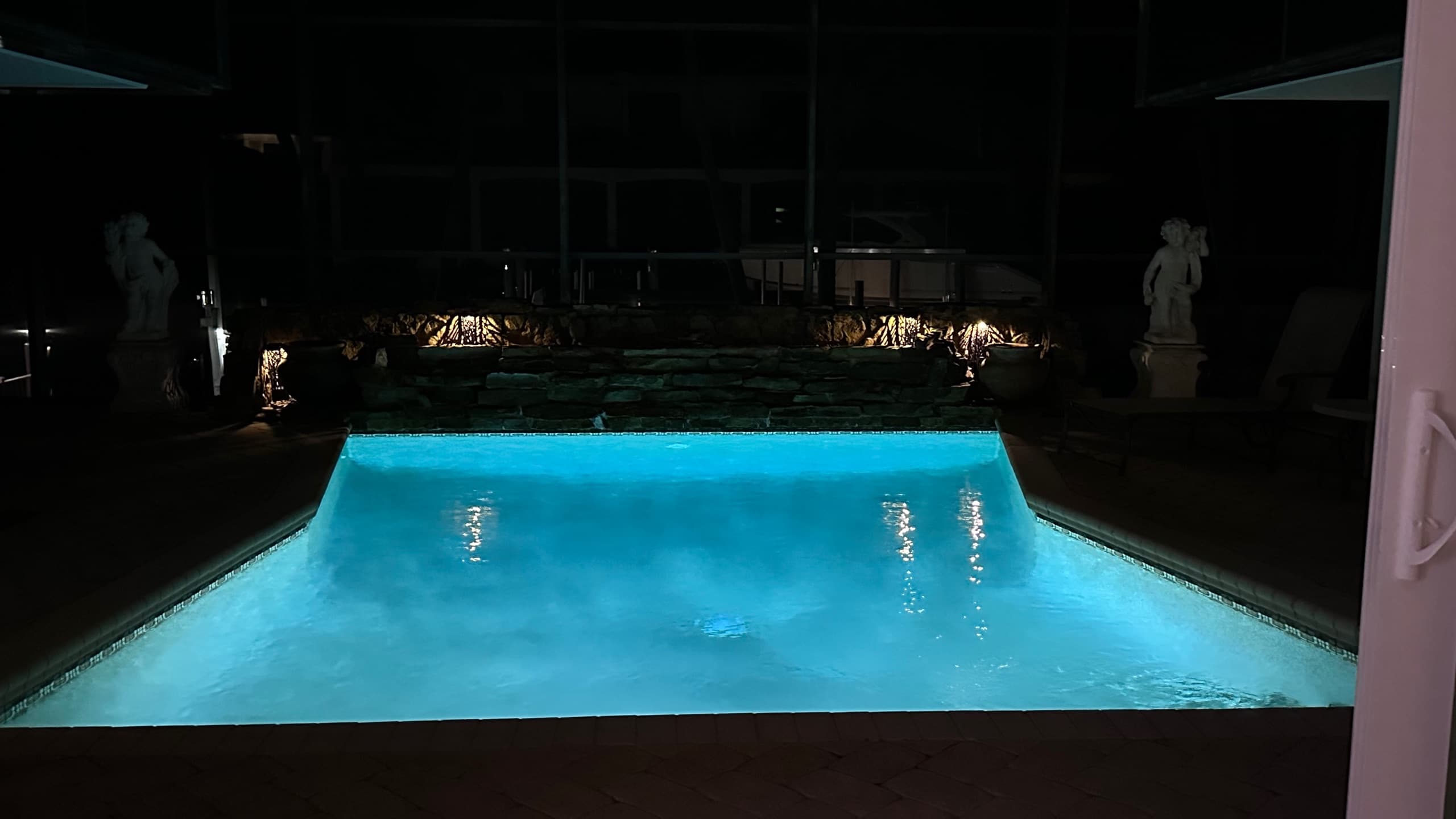 Pool glowing turquoise at night with the stone waterfall lit behind it
